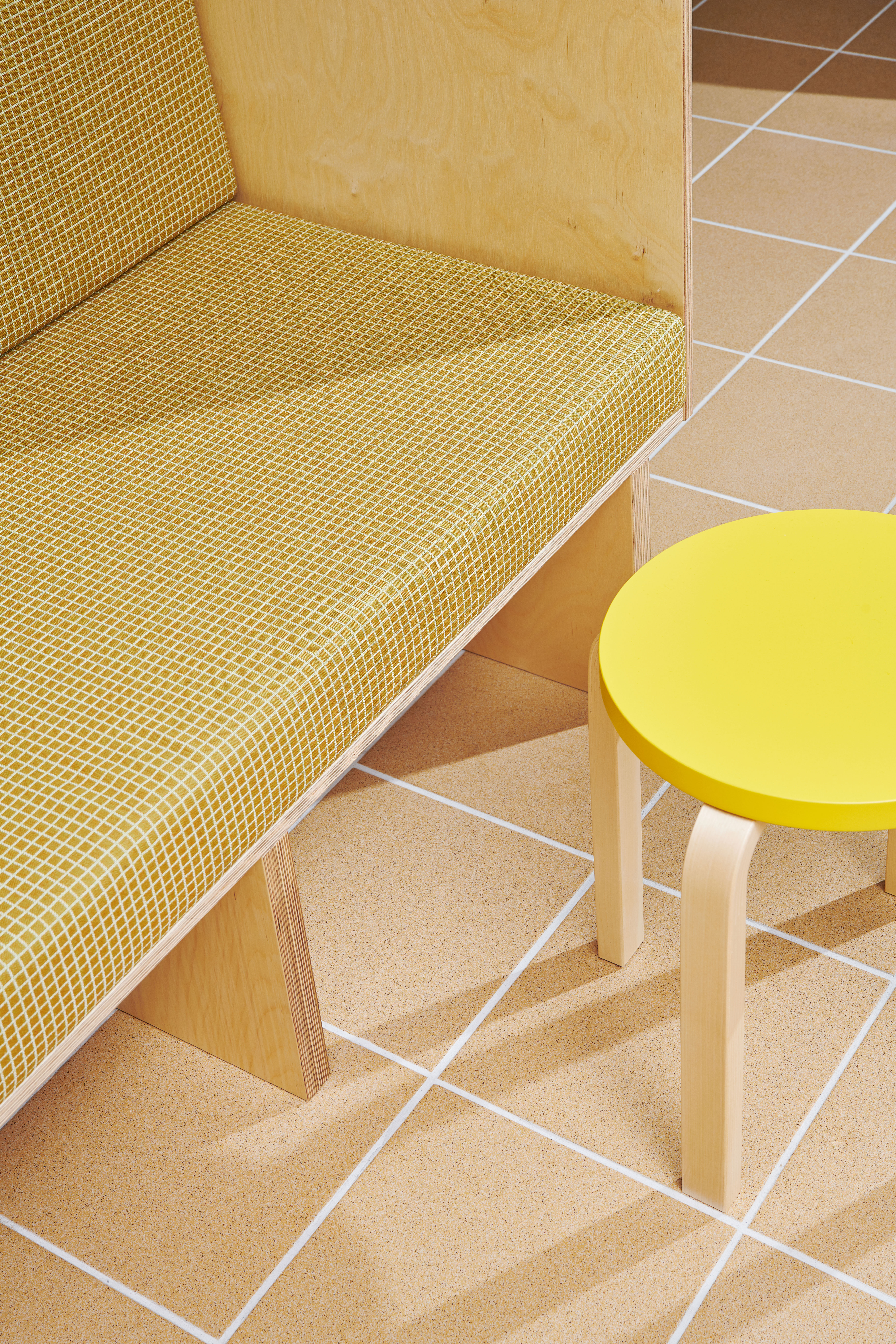 close-up of a yellow bench, pale yellow tiles and yellow artek stool with wooden legs