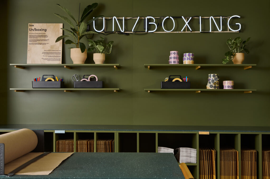 packing station in box by posti, dark military green walls and furniture, led sign "un/boxing"