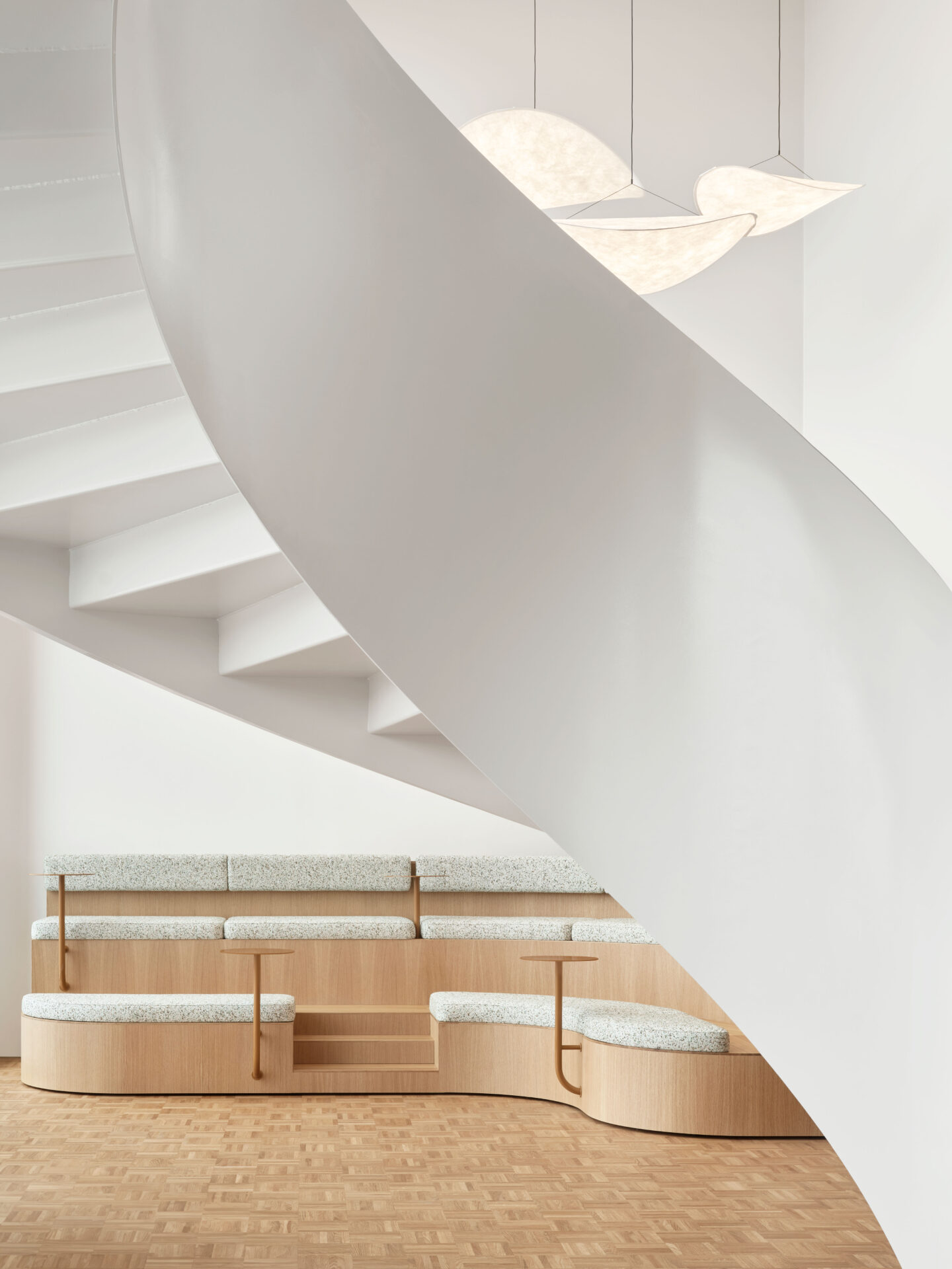 elegant white spiral staircase in front of a wooden bench with light upholstery and small side tables, modern office design