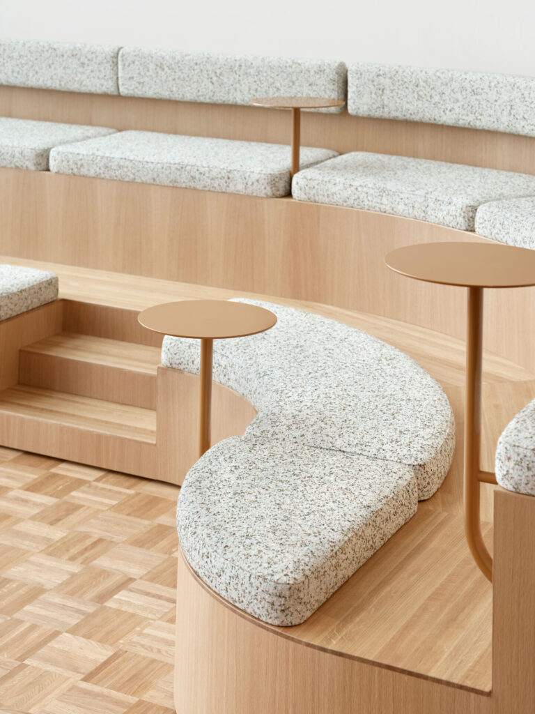 curved wooden seating office bench with light upholstered seating pillows, mounted round tables