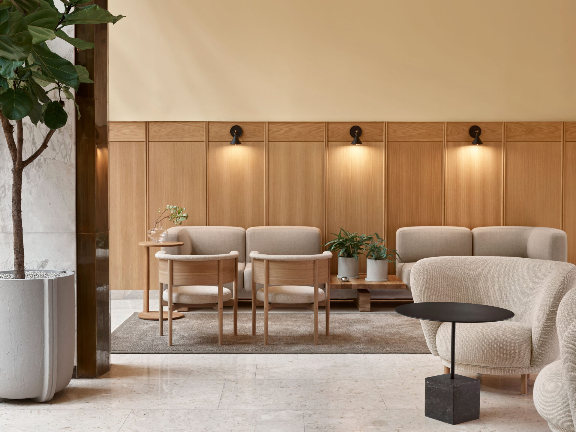 office lounge with light crème color furniture, wooden panels, black wall lights, a large plant on the left